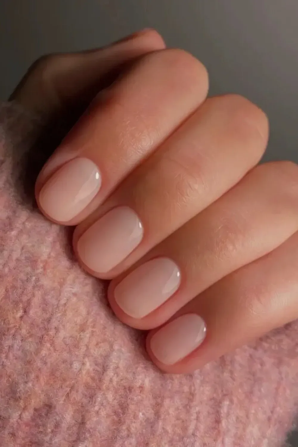 Simple Short Subtle Pink Milky Manicure - Everyday Luxury - Close-up of a hand with short, squoval-shaped nails covered in a high-shine, subtle pink milky sheer polish.