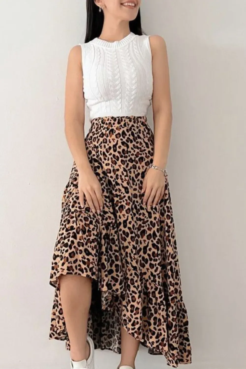 Leopard Print High-Low Ruffle Skirt Outfit	Woman wearing a white cable knit sleeveless top tucked into a high-waisted leopard print high-low midi skirt, styled with white sneakers.