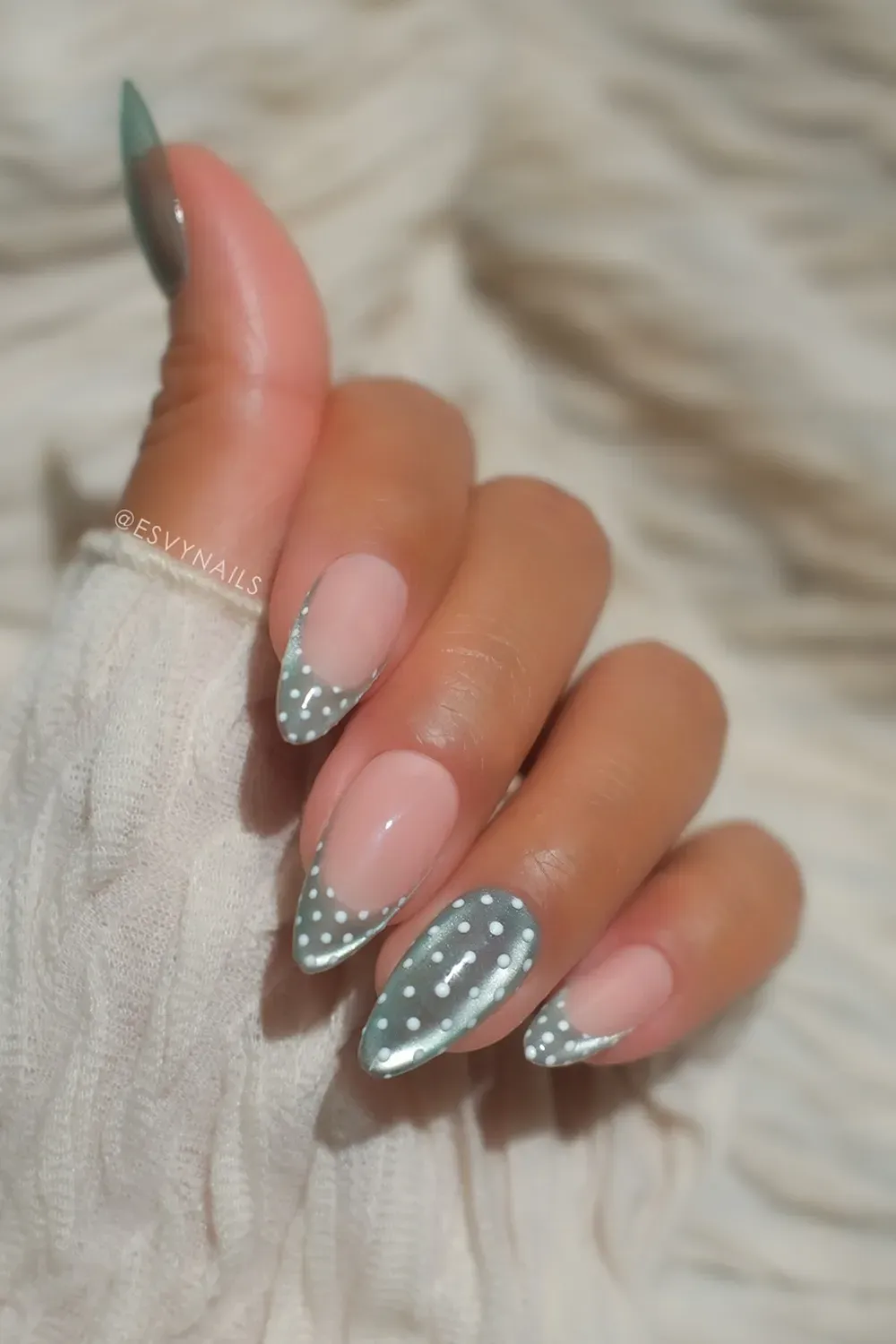 Long stiletto nails with a nude base and a metallic sage green French tip accented with small white polka dots.