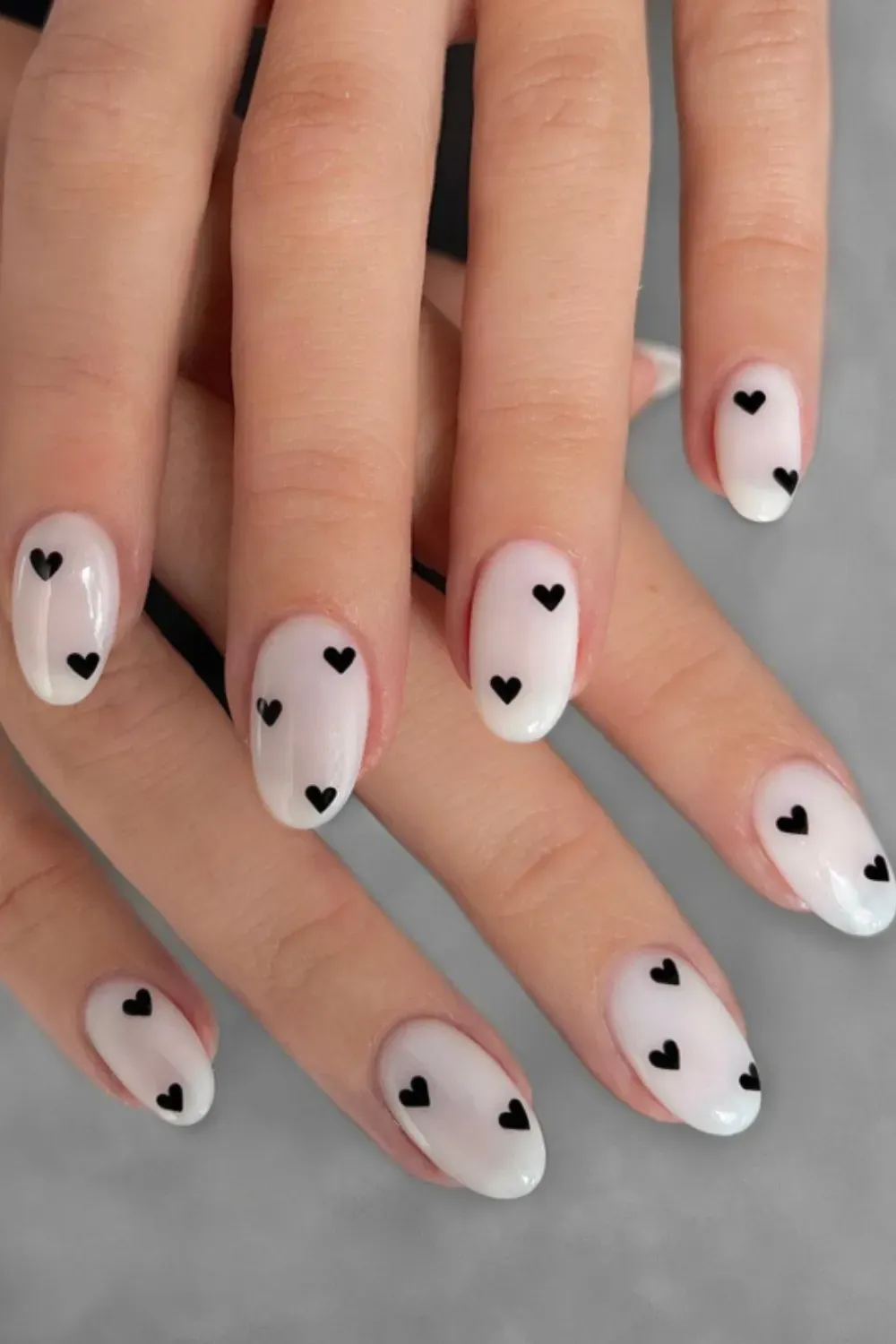 Milky Almond Nails Black Heart Art - Almond-shaped nails with a sheer milky white polish base and small, black heart designs on each nail.