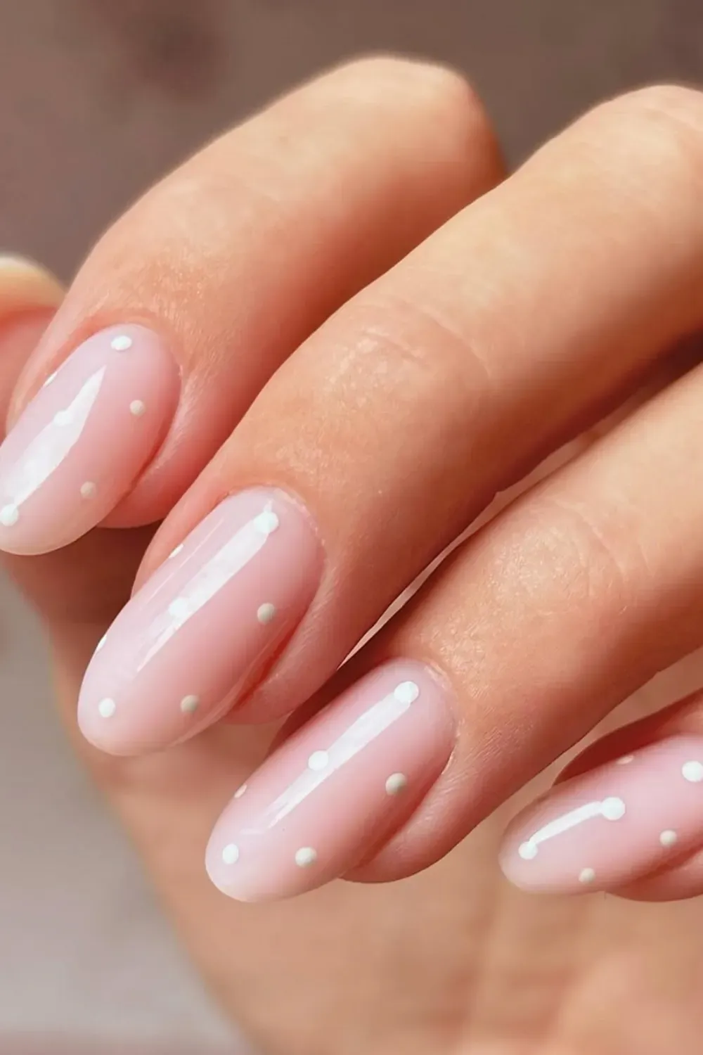 Oval nails with a milky, sheer pink base coat and sparse, small white polka dots for an understated, clean look.