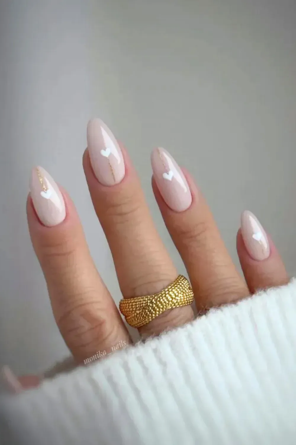 Milky Nude Nails with Gold Line and White Hearts - Almond-shaped nails with a nude milky base, accented with a vertical gold stripe and small white heart decals.
