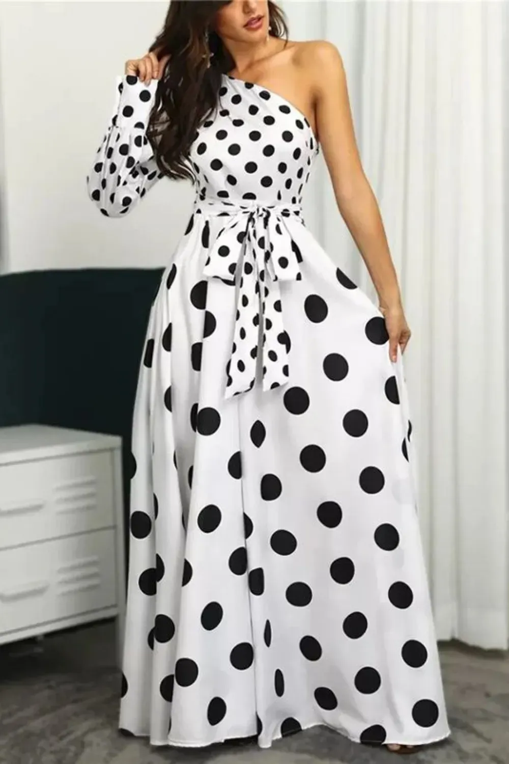 White One-Shoulder Polka Dot Maxi Gown	Woman in a white one-shoulder maxi dress with a full skirt, large black polka dots, and a matching fabric tie belt.