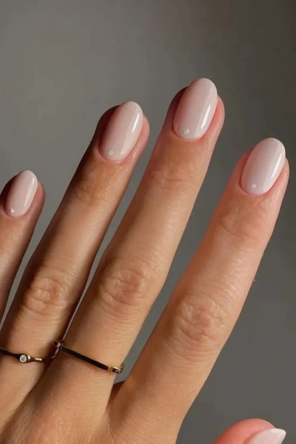 Short Milky Oval Nails White Dot Art - Short, oval-shaped nails with a pinkish-nude milky polish and a single white dot detail near the cuticle.