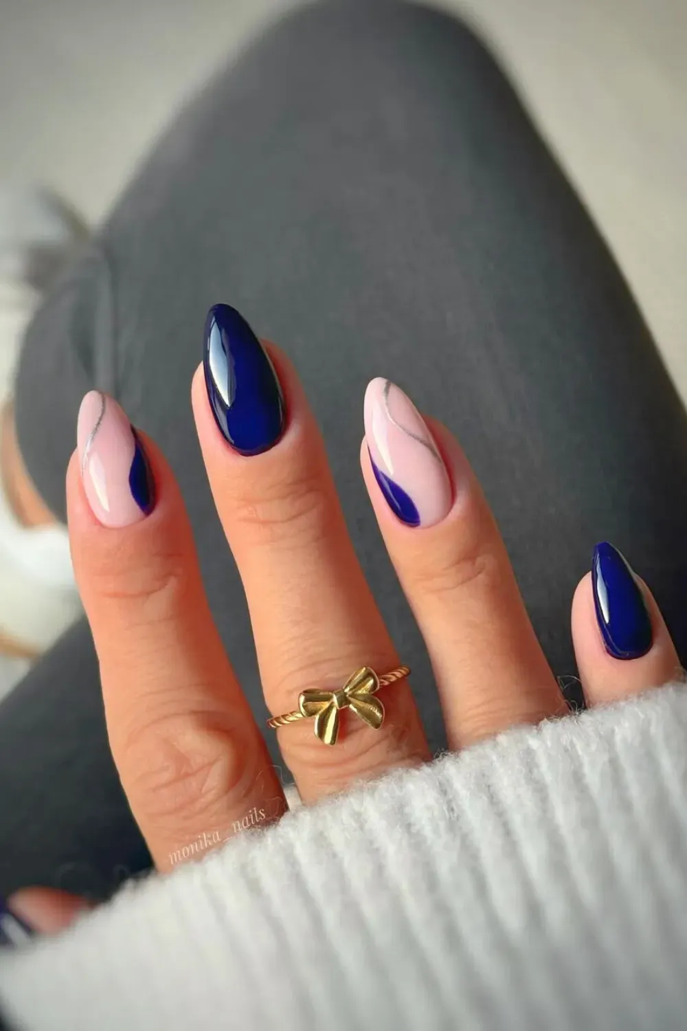 Abstract Blue Swirls with Nude and Silver Nails Almond nails featuring an abstract design with navy blue swirls, nude negative space, and a thin silver line accent, worn with a bow ring.