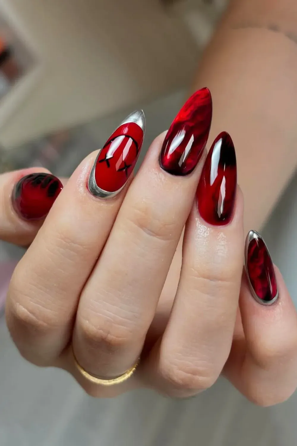 Stiletto nails with red and black abstract marble patterns, silver accents, and a red eye design on one nail.