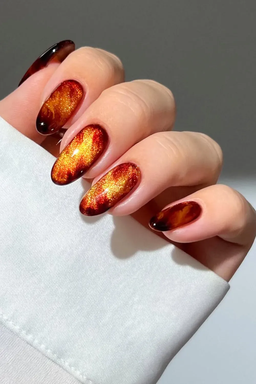 Warm amber and gold cat eye nails with dark brown/black ombre tips, resembling autumn flames.