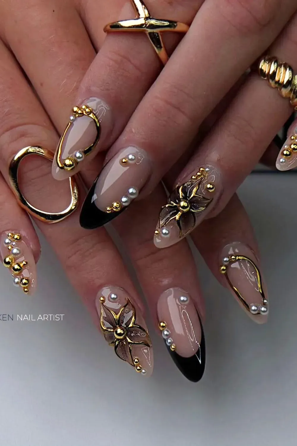 Nude nails with black tips and 3D gold floral accents.