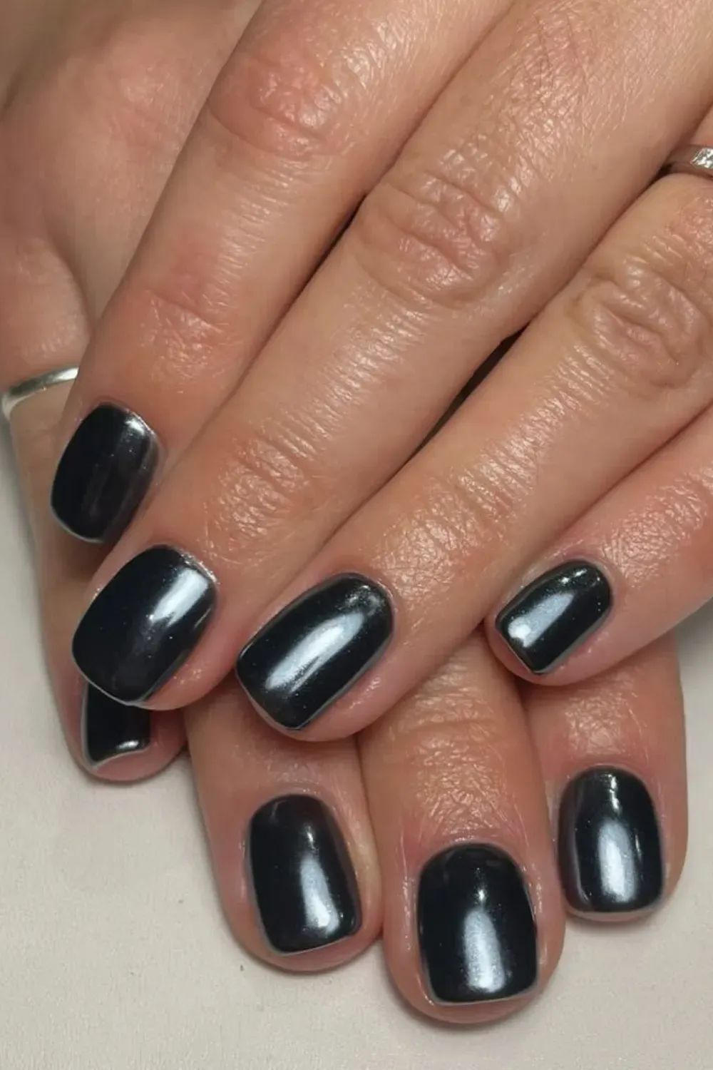 Hands wearing short, square-rounded nails coated in a highly reflective, metallic black chrome polish