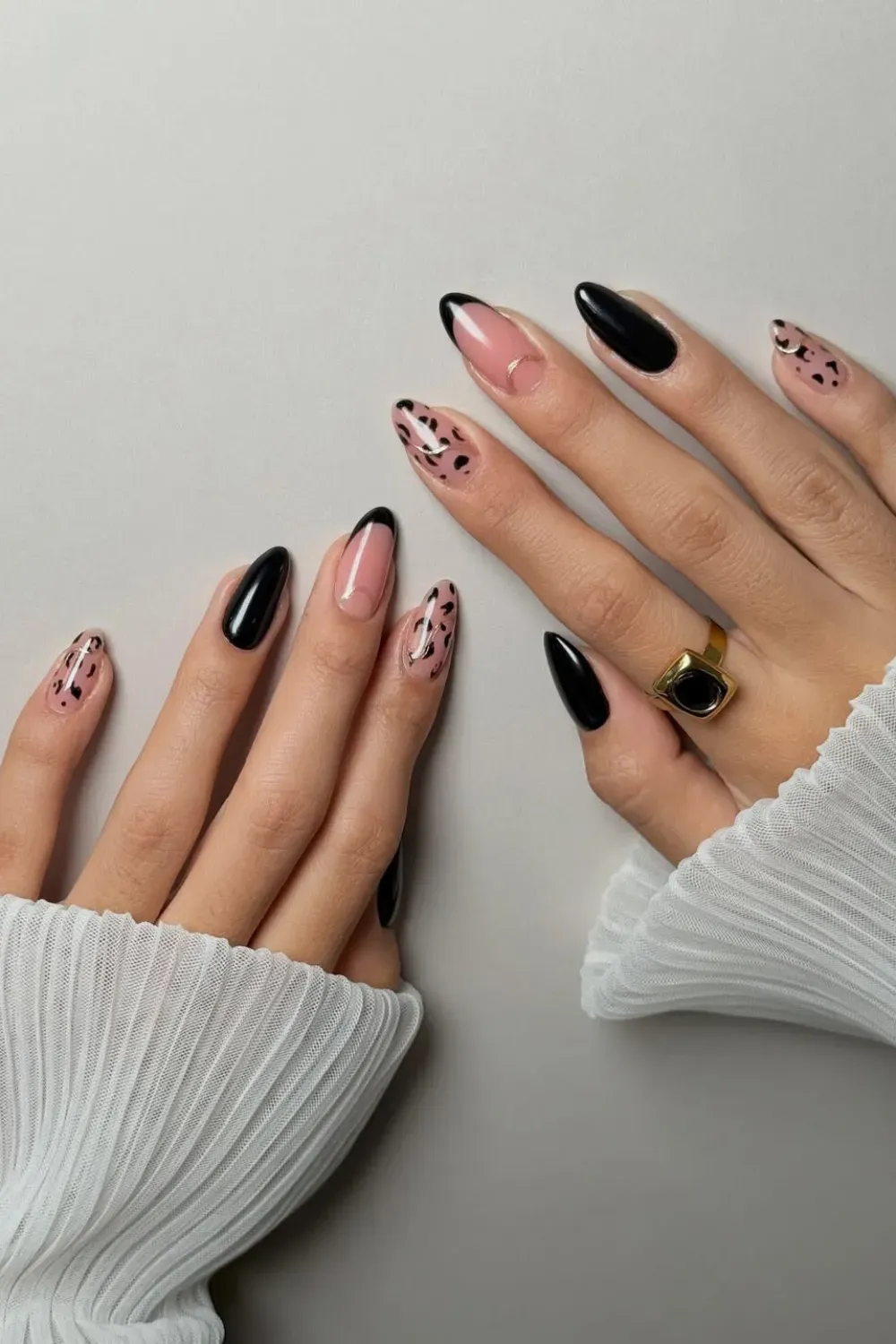 Almond nails alternating between solid glossy black, and a nude base with black French tips and black leopard/dalmatian print spots.