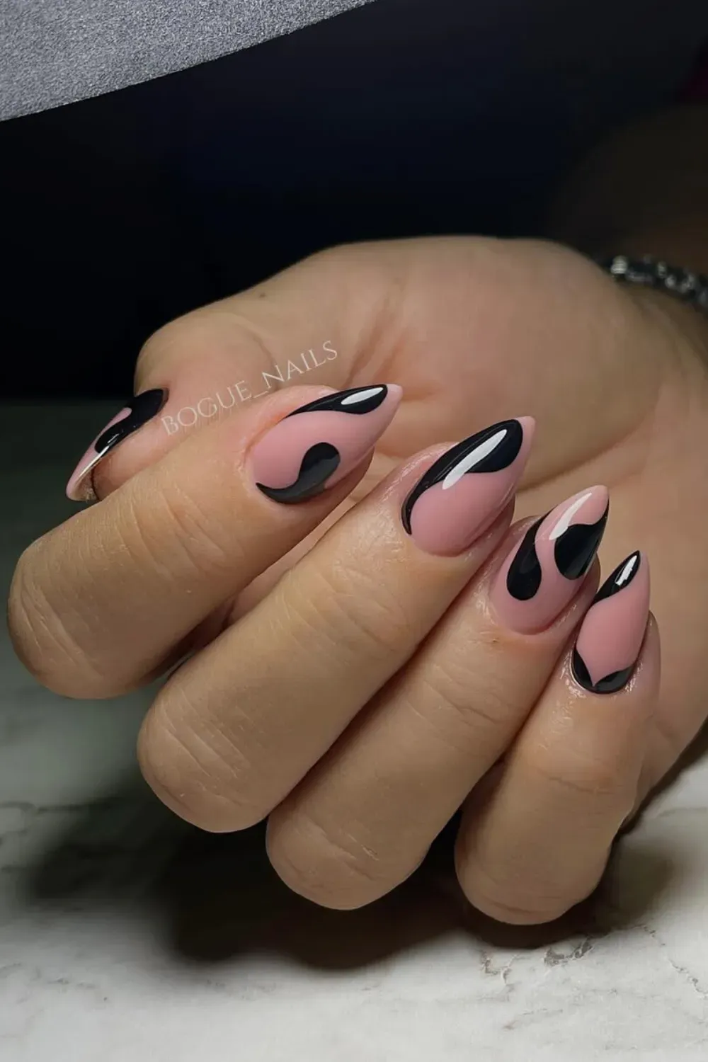Almond-shaped nails with a nude base featuring thick, glossy black abstract, wavy shapes and negative space.