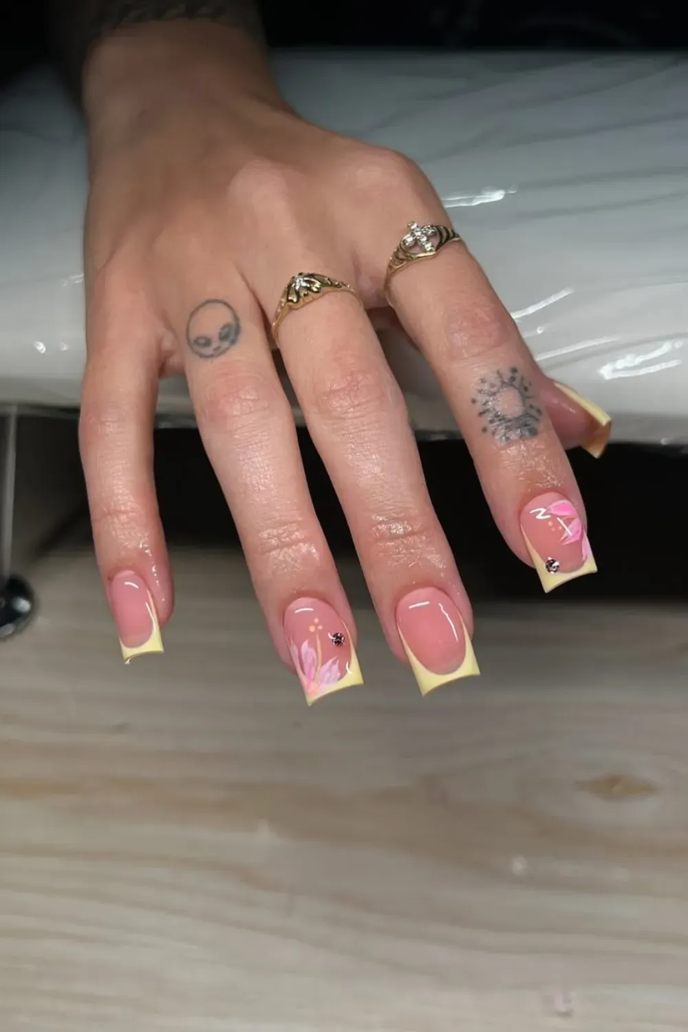 Long square nails with a pastel yellow French tip and hand-painted pink and white floral designs on an accent nail.
