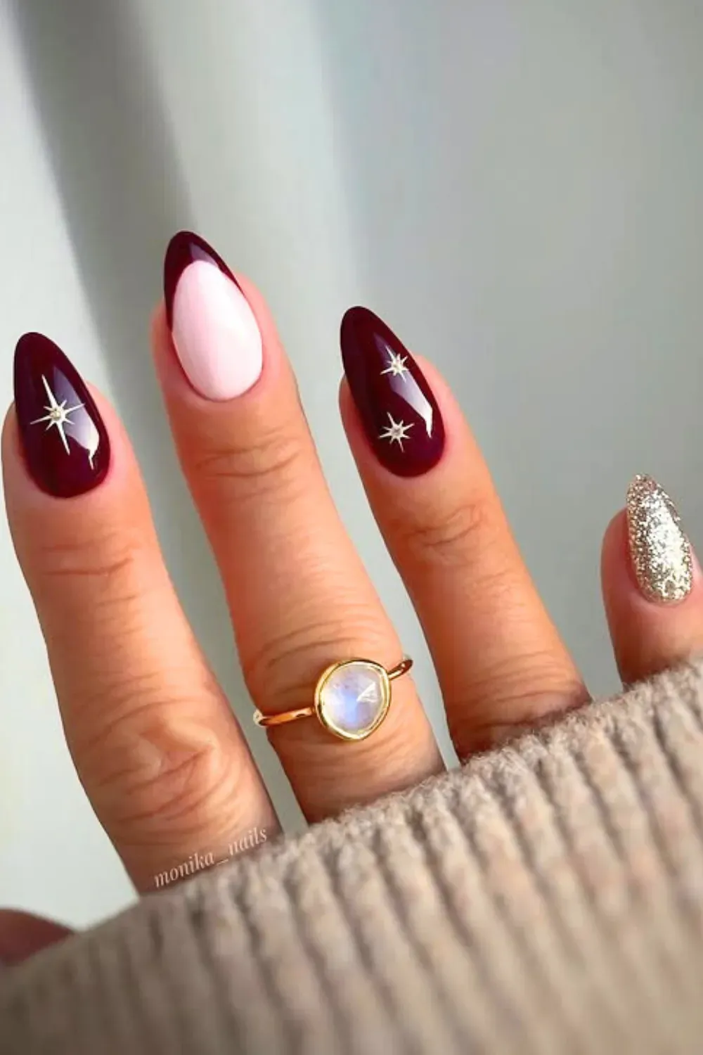 Almond-shaped nails with burgundy starburst designs, a light pink accent nail, and one covered in silver glitter.