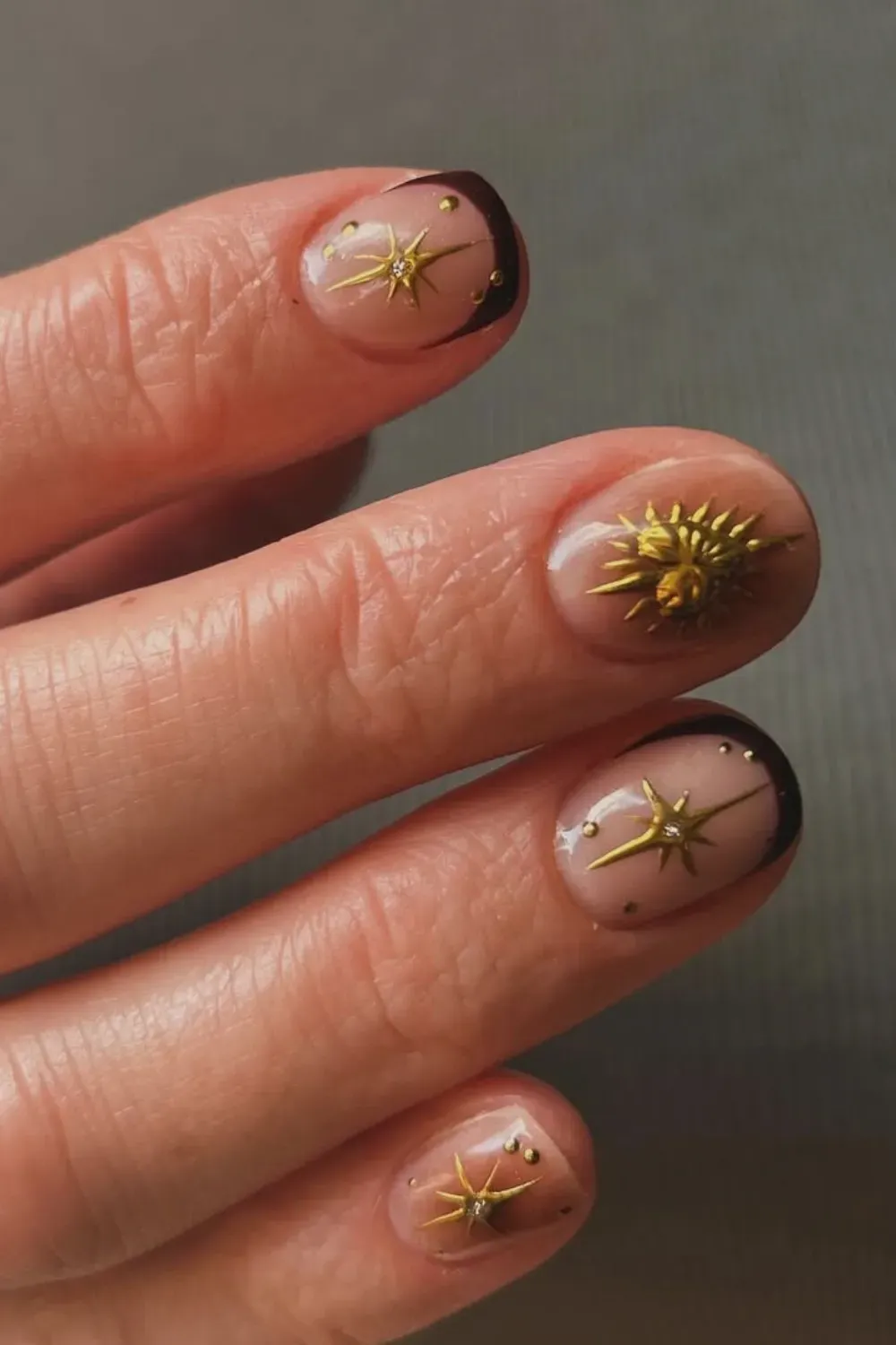 Short oval nails with a dark brown French tip and 3D gold celestial sun and star charms with gold dots.
