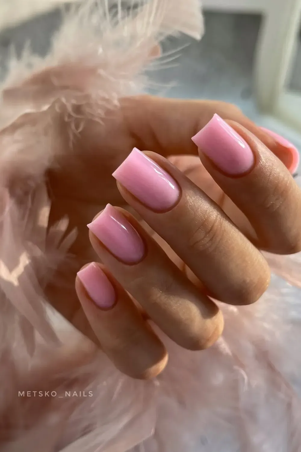 Hand holding a pink feather boa, showing short square nails painted in a solid, glossy bubblegum pink.