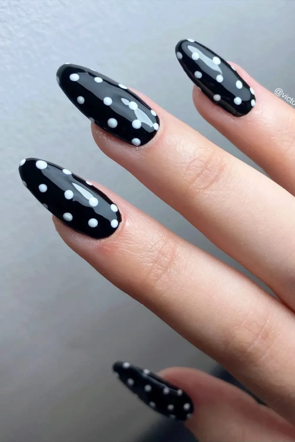 Hand with long oval black nails with uniform white polka dots.