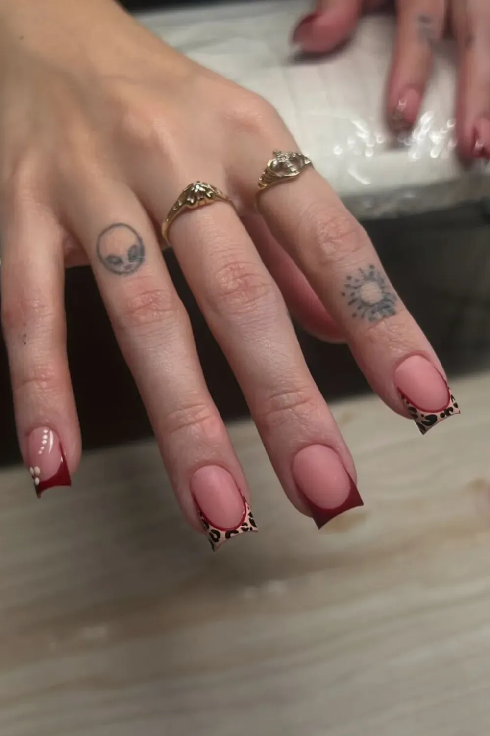 Long square nails with a nude base, deep red tips, and subtle leopard print detail on the sides.