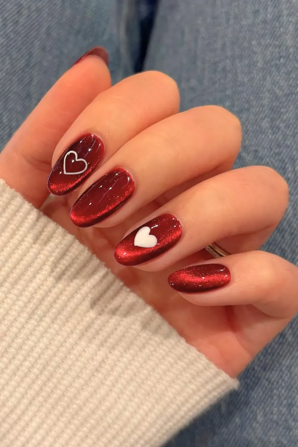 Deep red velvet cat eye nails with a glossy finish and white heart nail art on an oval shape.