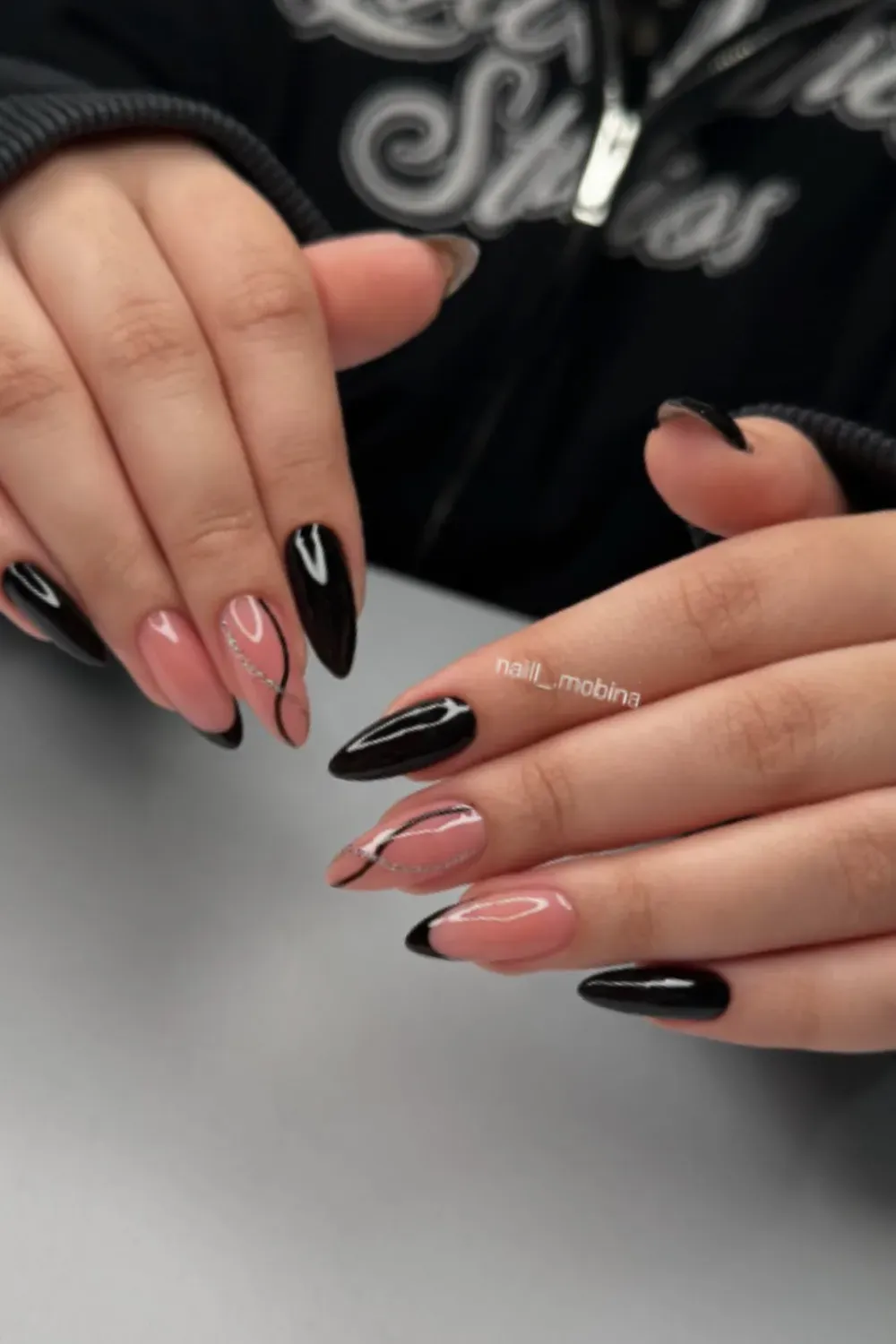 Pointed oval nails alternating between solid glossy black and a sheer nude base with a thin black and silver abstract swirl design