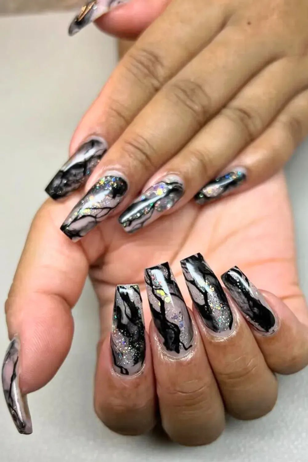 Edgy Marble with Glitter: Coffin-shaped nails featuring dramatic black and grey marble effects with sparkling iridescent glitter, offering a dark glam look.