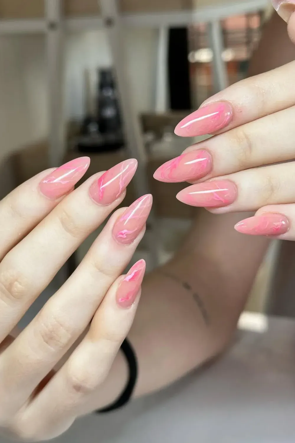 Two hands with long, glossy almond-shaped light pink nails featuring darker pink swirling designs.