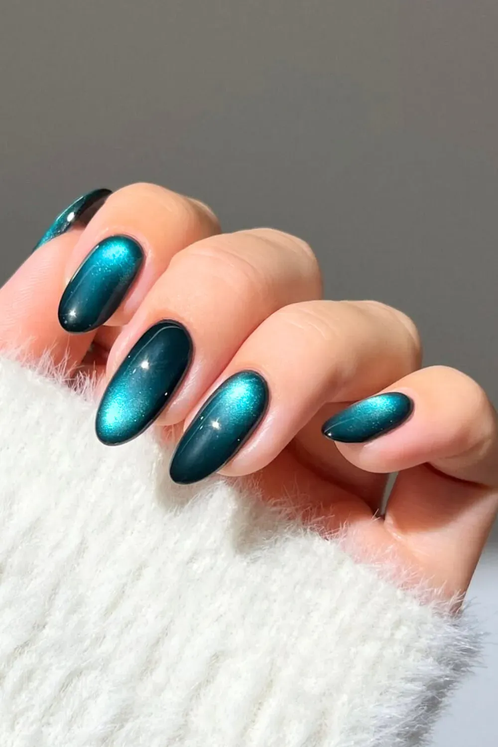 Close-up of glossy, deep emerald green cat eye nails on a tapered almond shape.