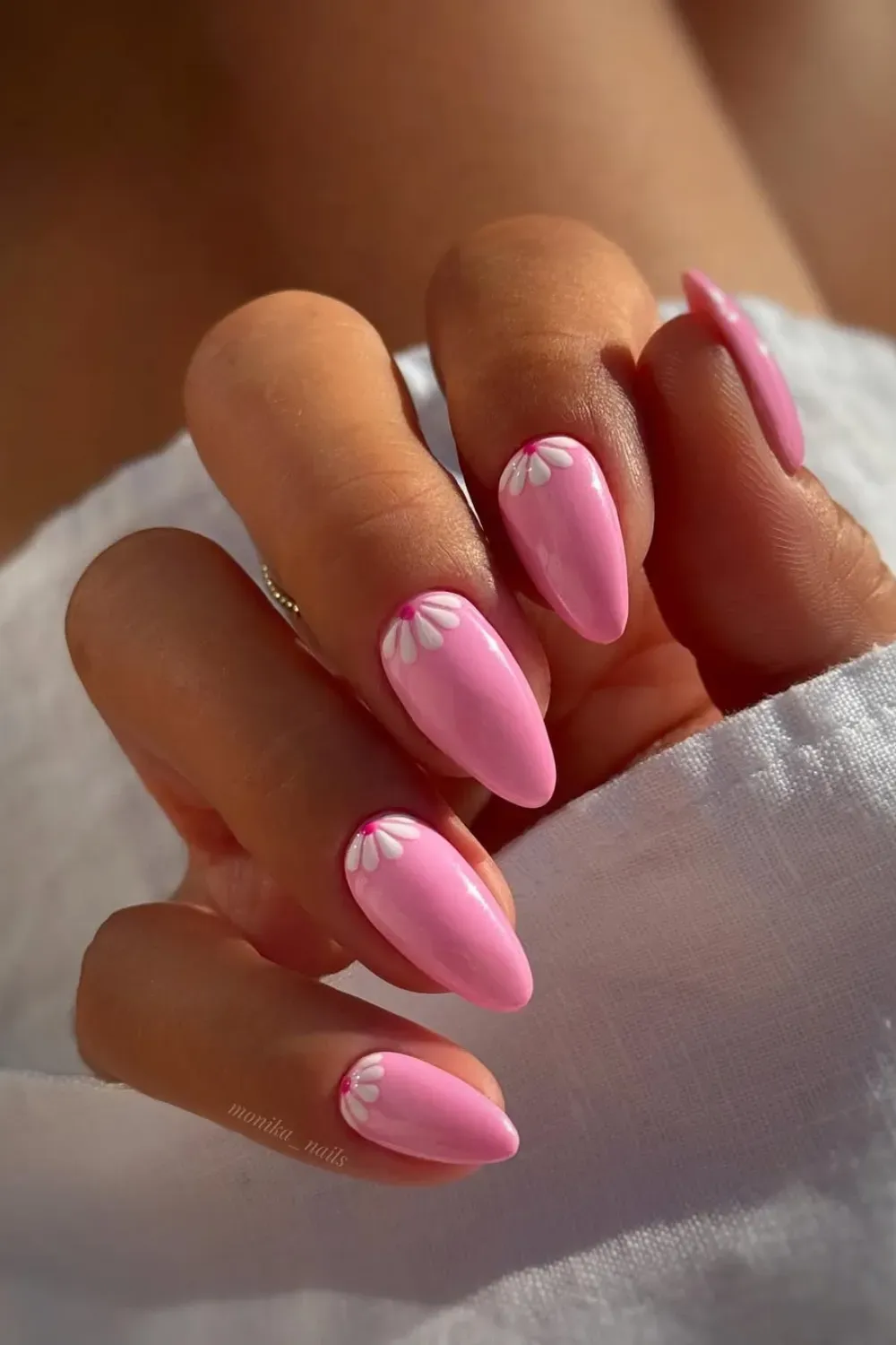 Hand with bright pink almond-shaped nails, each decorated with a small white daisy flower at the cuticle.