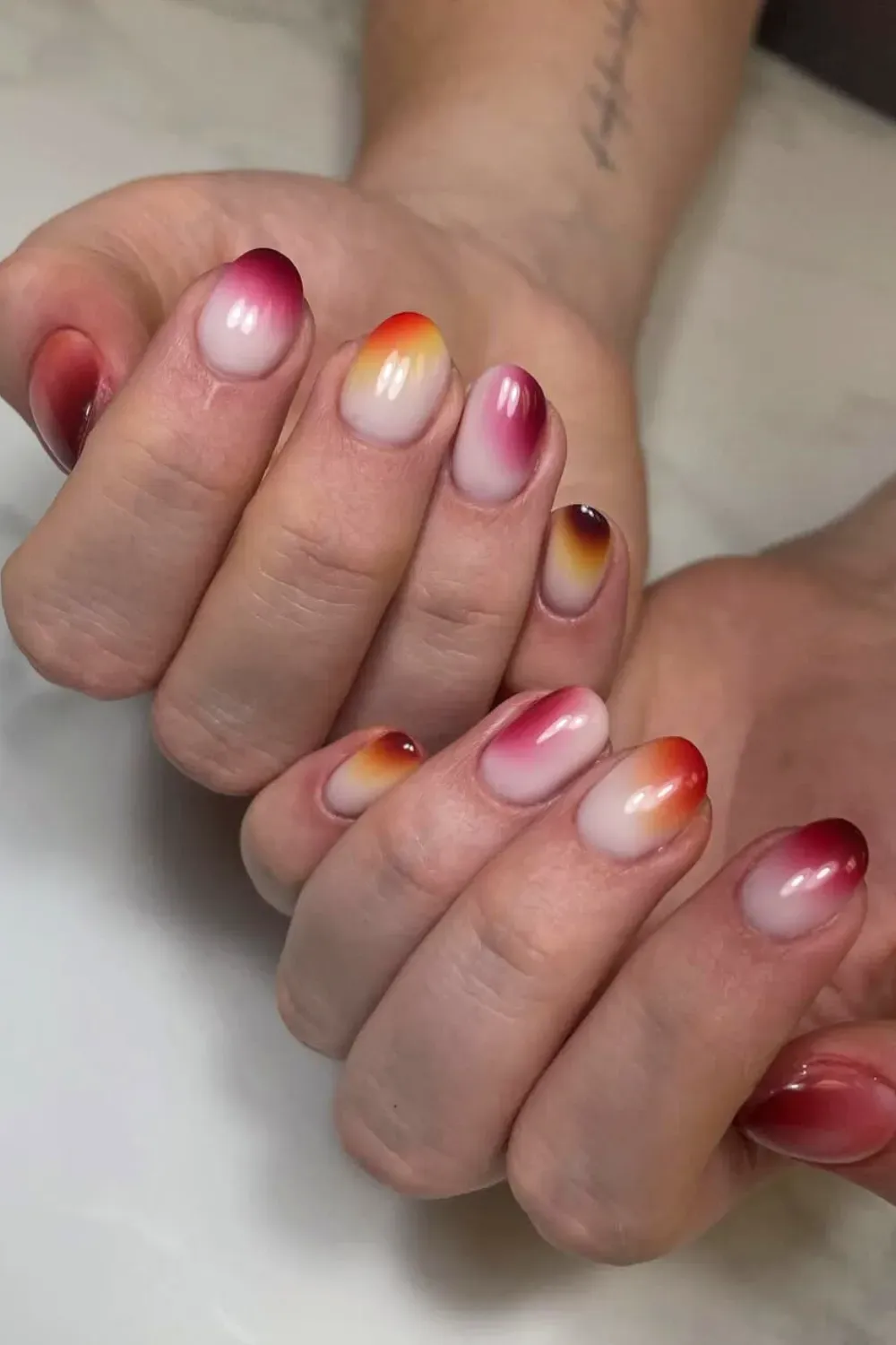 Oval-shaped nails showing a stunning gradient from white to orange, pink, and deep burgundy tips.