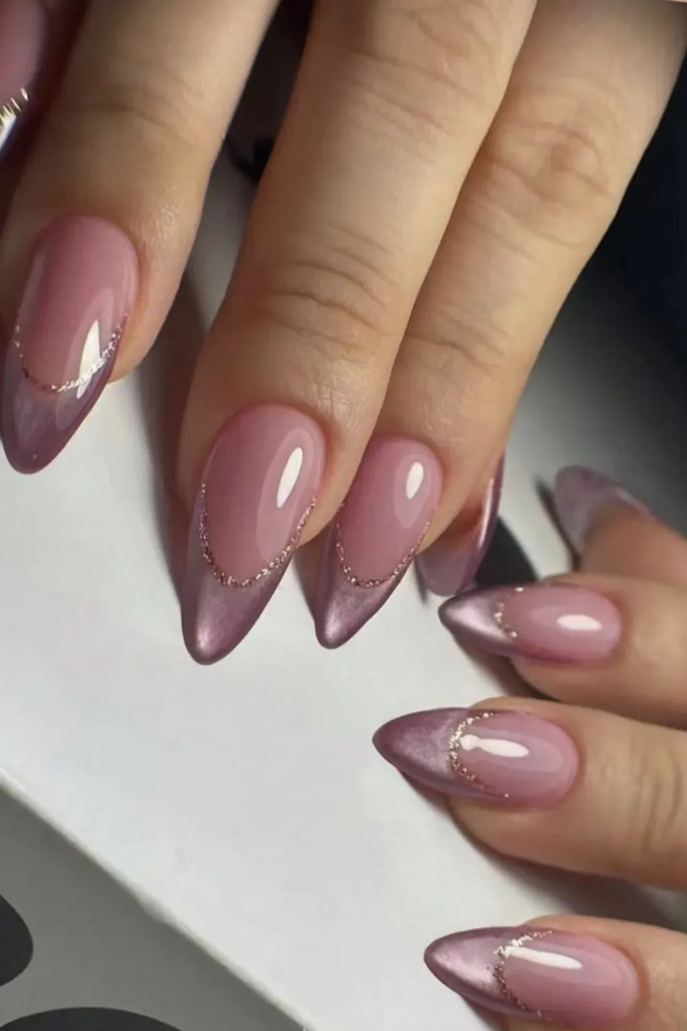 Pointed almond nails with a pink cat eye V-tip and a thin, sparkling gold glitter line accent.