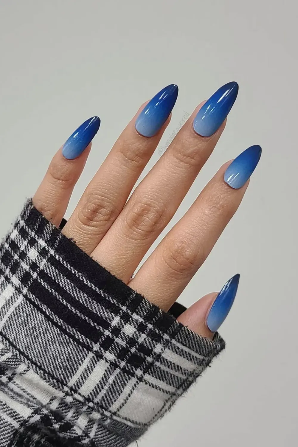 High-Gloss Blue Ombre Stiletto Nails Hand wearing a plaid sleeve showing long, glossy stiletto nails with a dark blue to light blue ombre effect.
