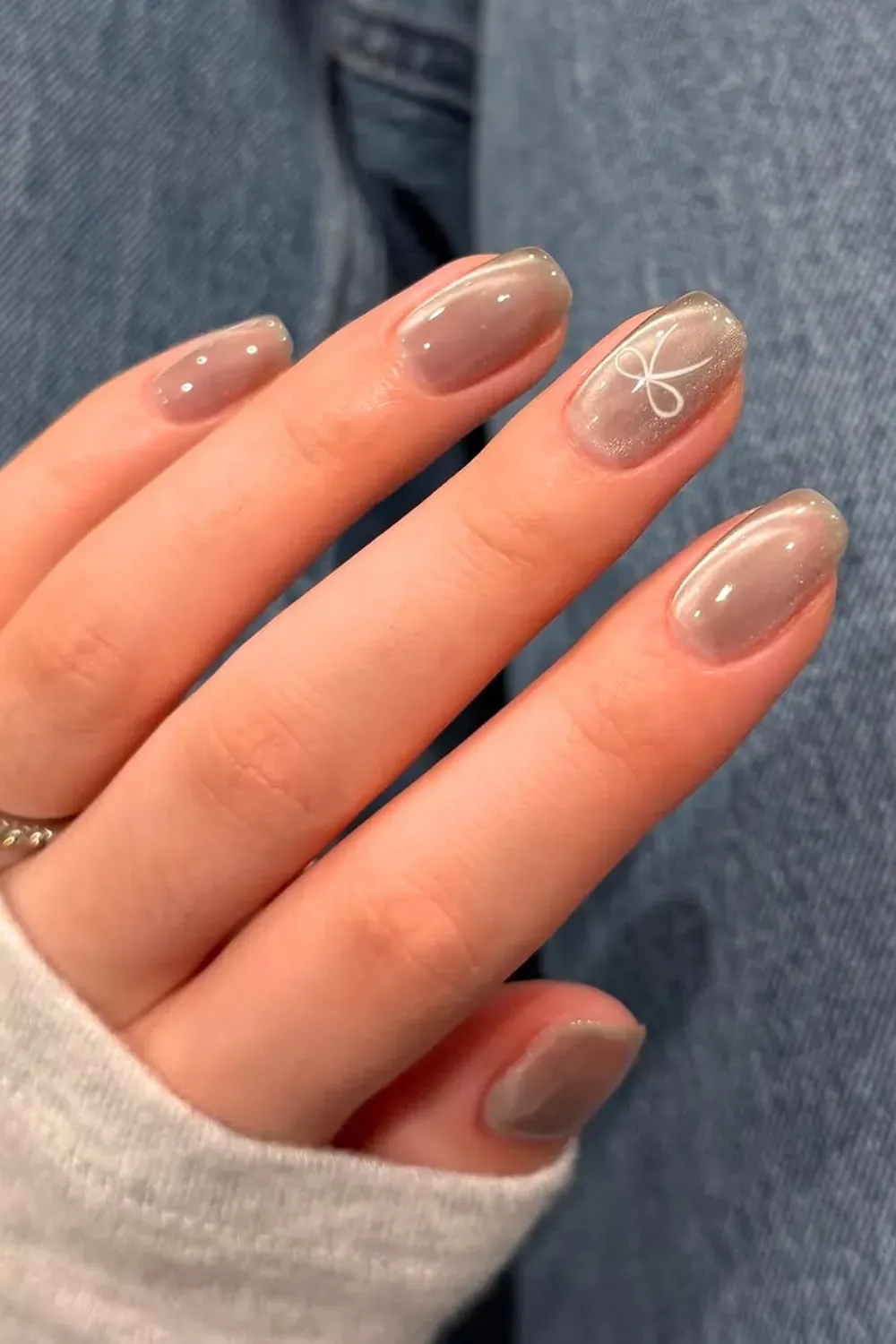 Sheer taupe glass cat eye nails with a delicate white ribbon line art on a short oval shape