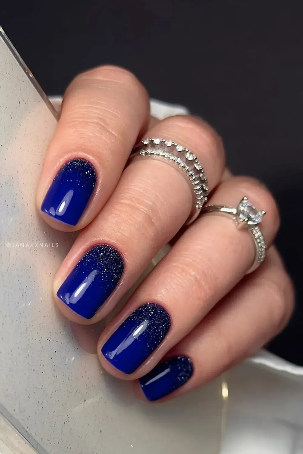 Navy Blue Glitter Accent Square Nails Square nails painted in a glossy deep navy blue with dark glitter accenting the cuticle line on all fingers.
