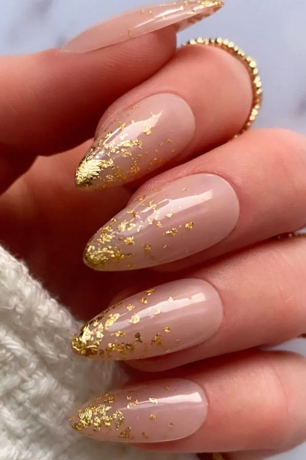 Nude almond nails with gold foil flakes on tips, distressed effect.