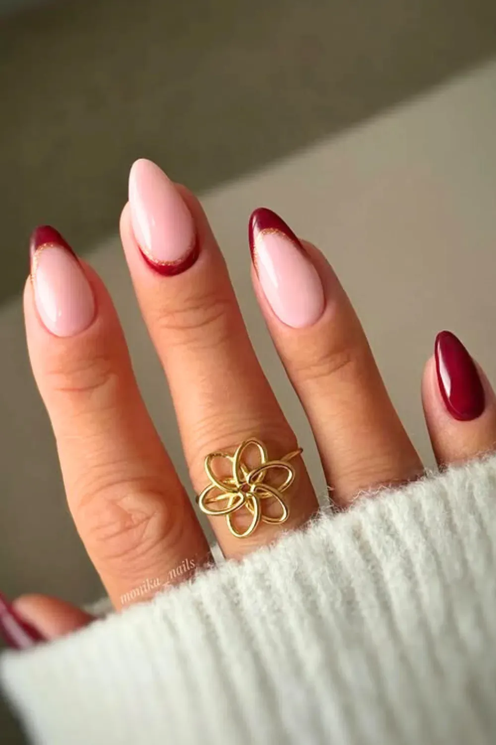 Almond-shaped nails featuring nude bases with burgundy French tips outlined in gold, along with a solid burgundy accent nail.