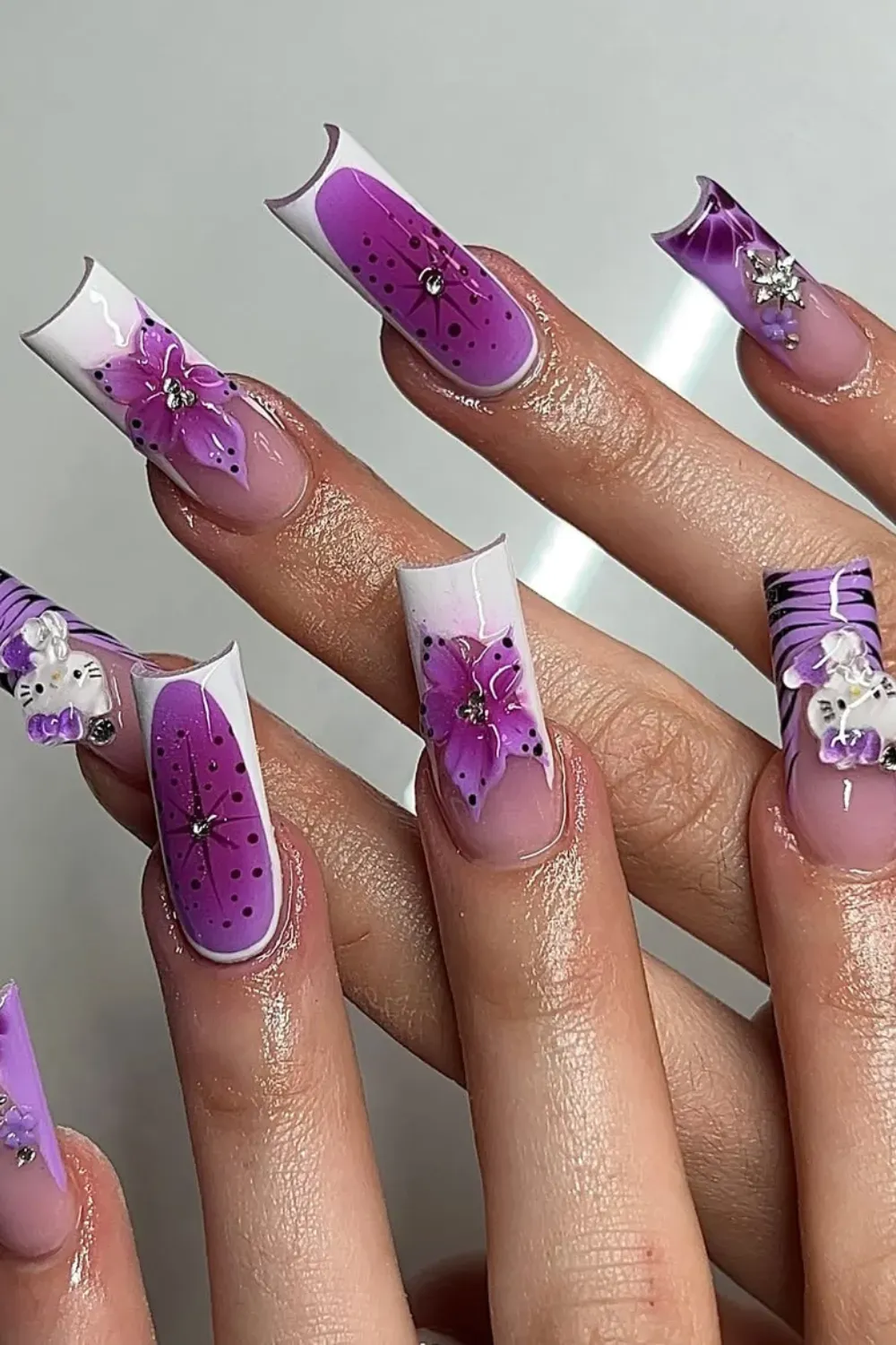 Maximalist Purple Hello Kitty Nails - Extreme square acrylic nails with rich purple airbrushed flowers, 3D Hello Kitty charms, and rhinestone accents.