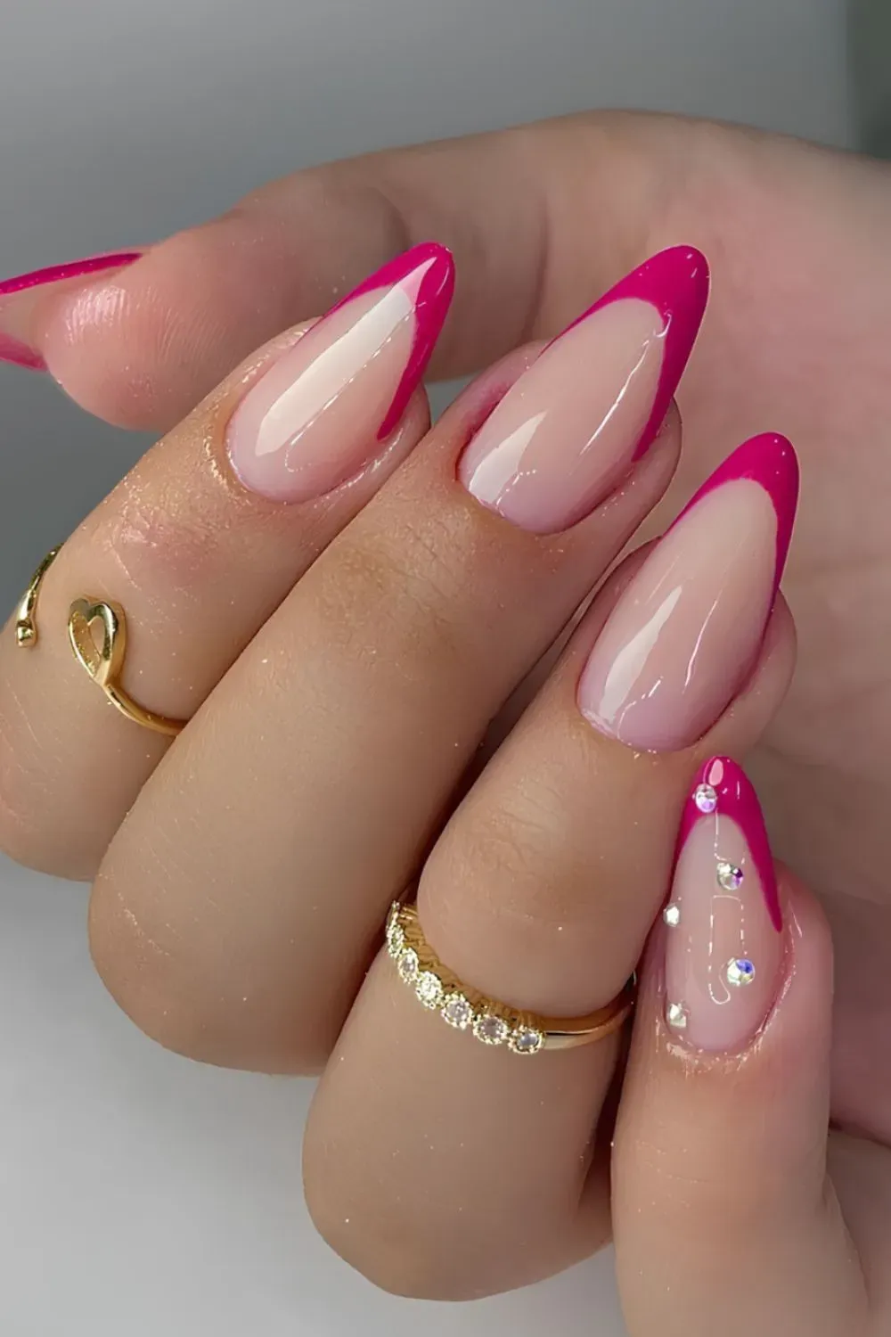 Nude base nails with hot pink French tips and rhinestone accents.