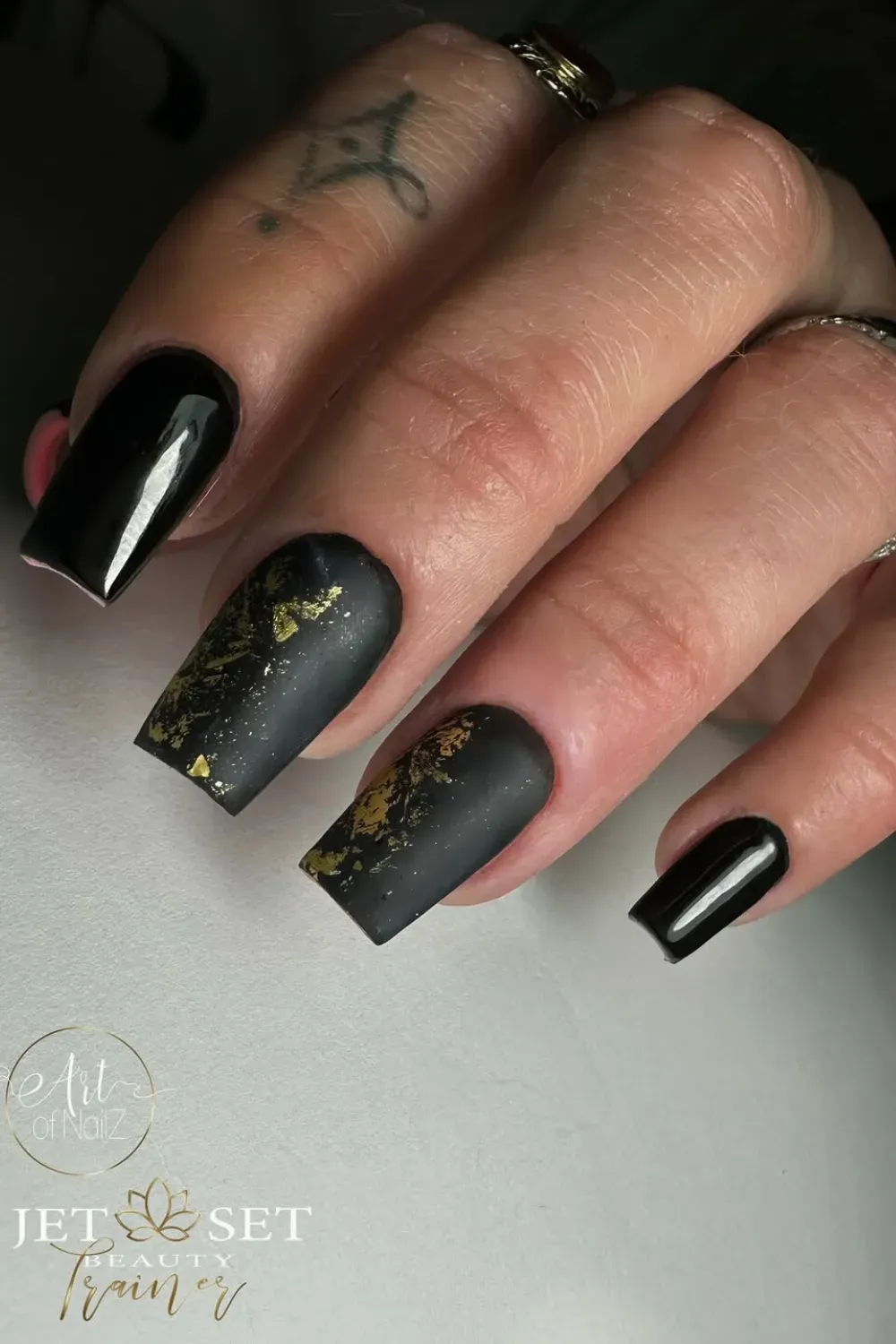 Close-up of coffin-shaped nails featuring a matte black finish, with two accent nails having scattered gold foil flakes over the matte black.