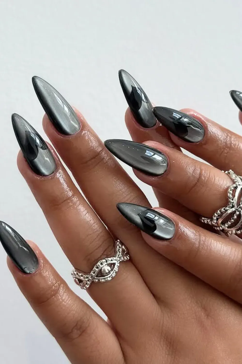 Long, stiletto-shaped nails with a dark metallic charcoal cat eye effect and reflective finish.