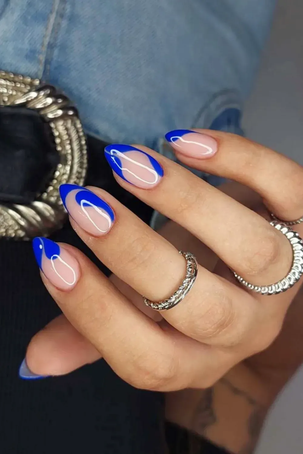 Blue Negative Space Swirl French Manicure Almond nails with a nude base featuring a flowing, abstract blue swirl design that outlines a modern French tip.