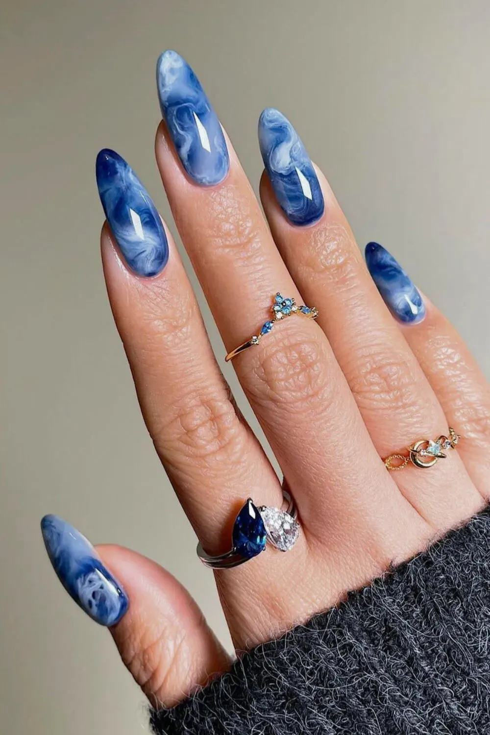 Blue and White Marble Ocean Wave Nails Long almond nails showcasing a stunning blue and white marble effect, resembling ocean waves, worn with multiple rings.