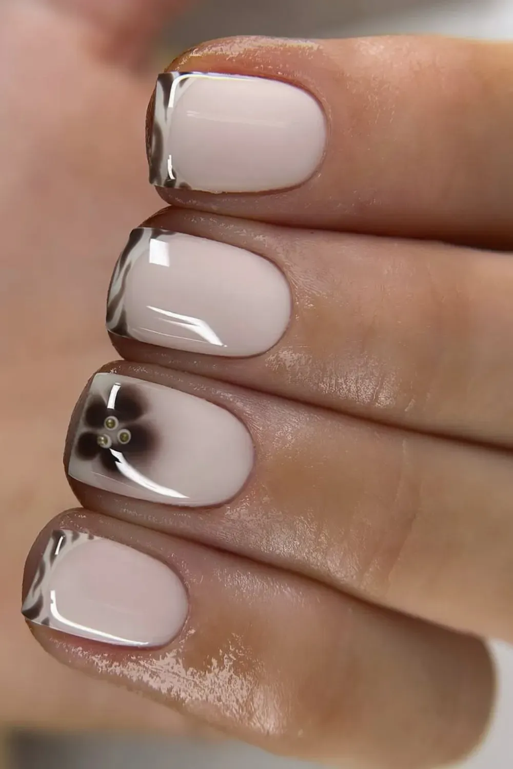 Short oval nails with a brown and white wavy zebra-print French tip and a soft brown ombré flower on an accent nail.