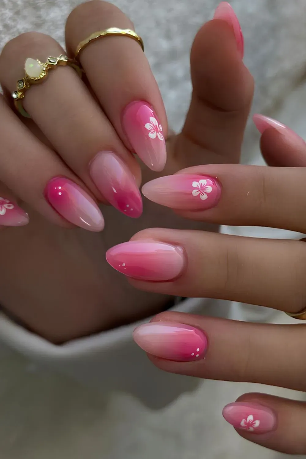 Pink ombre nails with white flower details on almond-shaped nails.