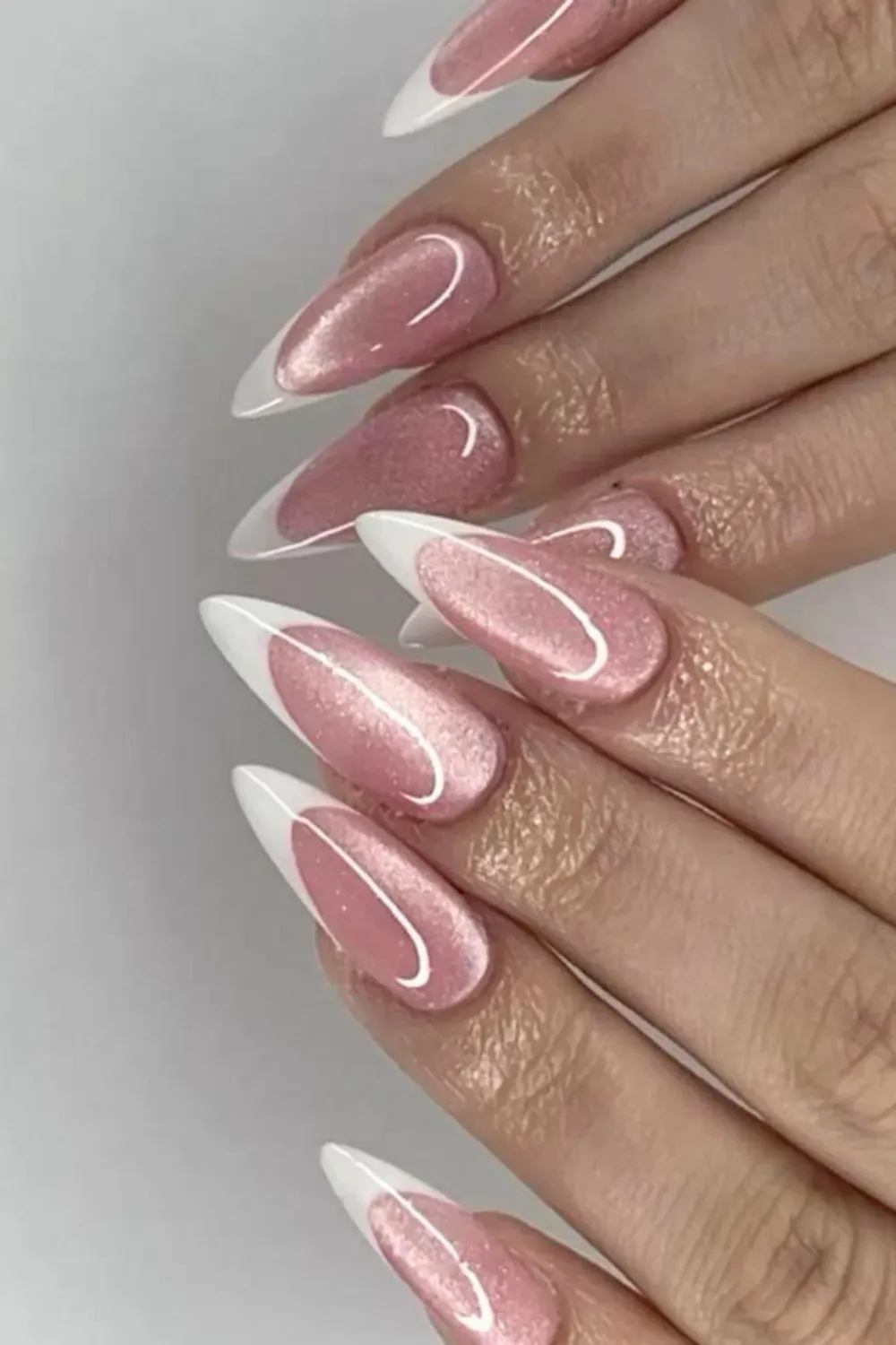 Pink shimmer cat eye nails with a sharp white French tip on a long almond nail shape.