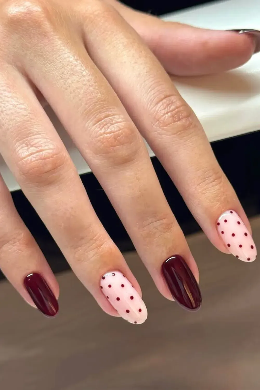Oval-shaped nails with a mix of solid burgundy and translucent nude nails featuring small burgundy polka dots.
