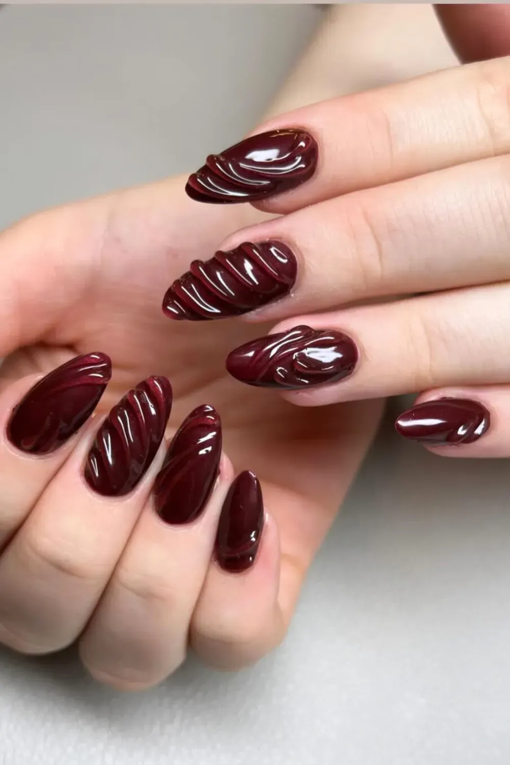 Long oval-shaped nails with raised burgundy swirl patterns, adding texture and depth to the glossy finish.