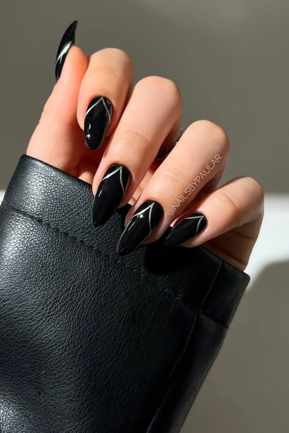 Long, pointed stiletto nails painted glossy black with thin silver geometric V-lines near the tip.