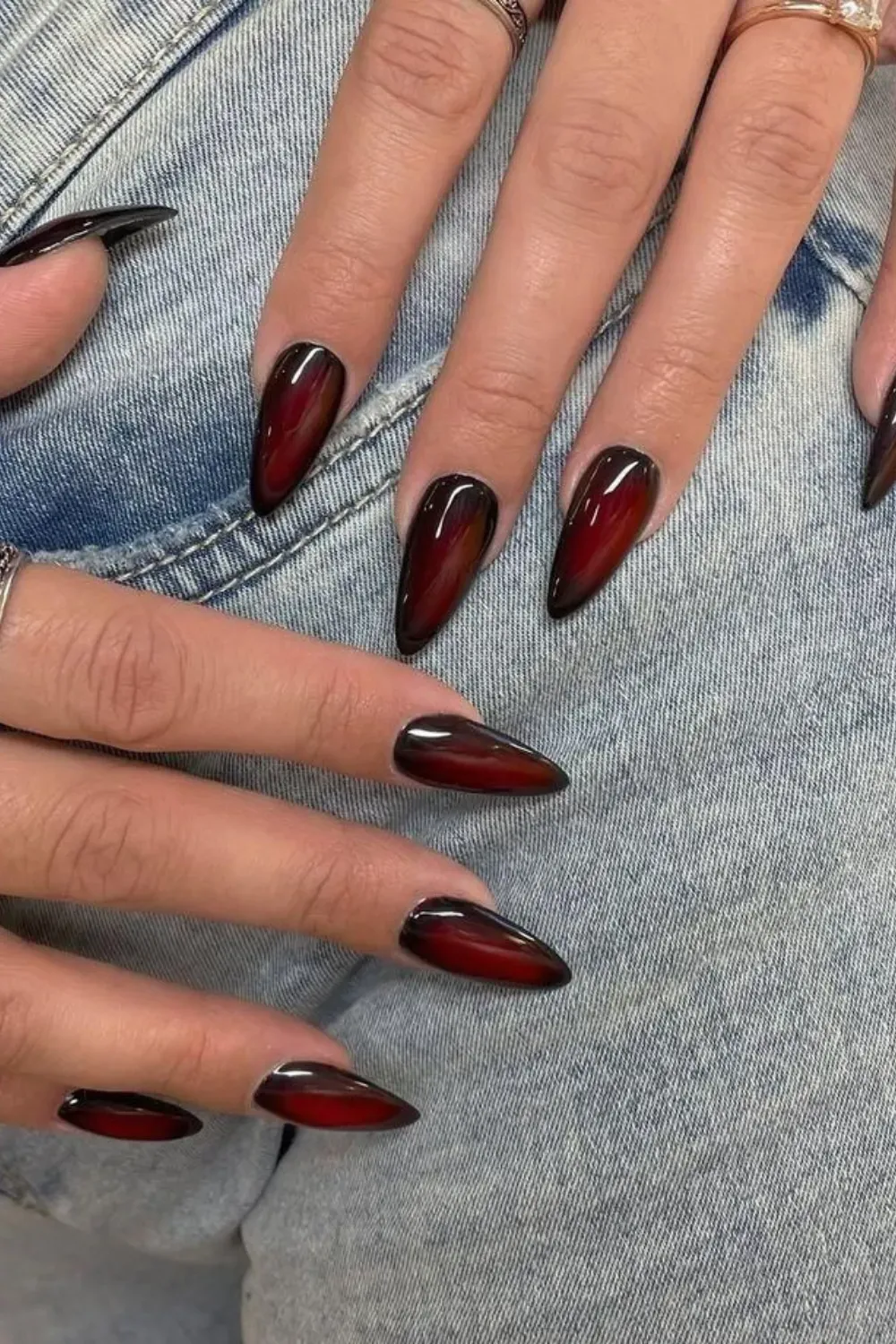 Two hands with long stiletto nails featuring a smoky ombre gradient from deep red to dark black tips.