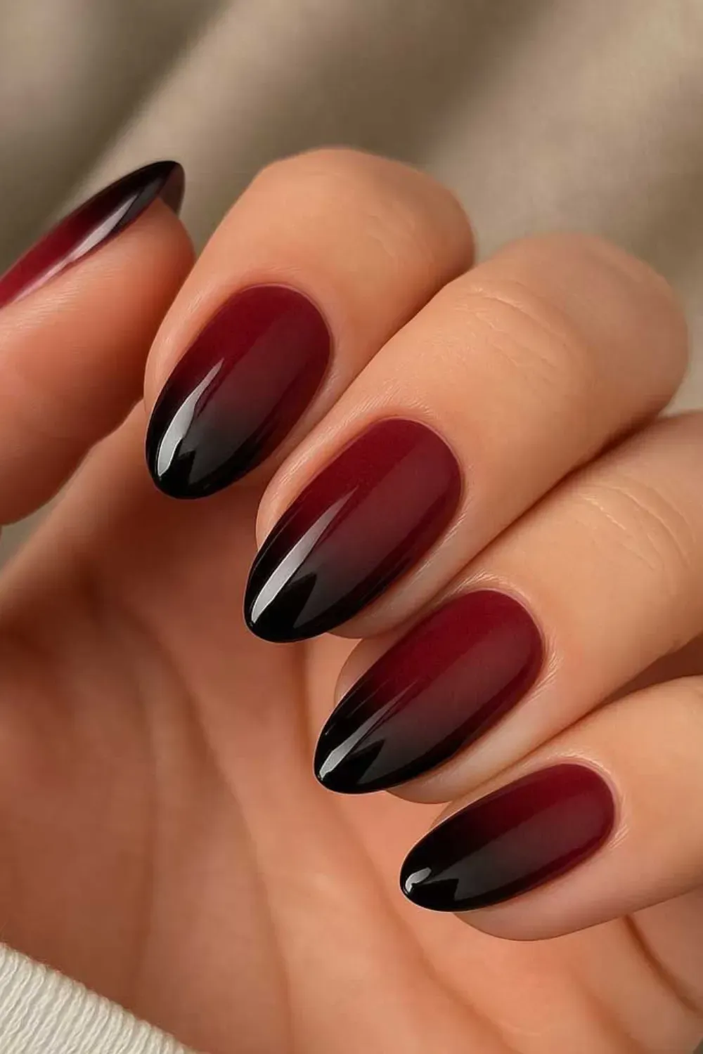 Hand with oval-shaped nails featuring a striking ombre gradient from deep burgundy at the base to black at the tips.