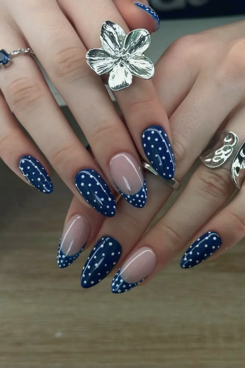 Navy Blue Polka Dot Almond Nails with Rings Almond nails featuring a navy blue base with white polka dots and a negative space half-moon accent, decorated with silver rings.
