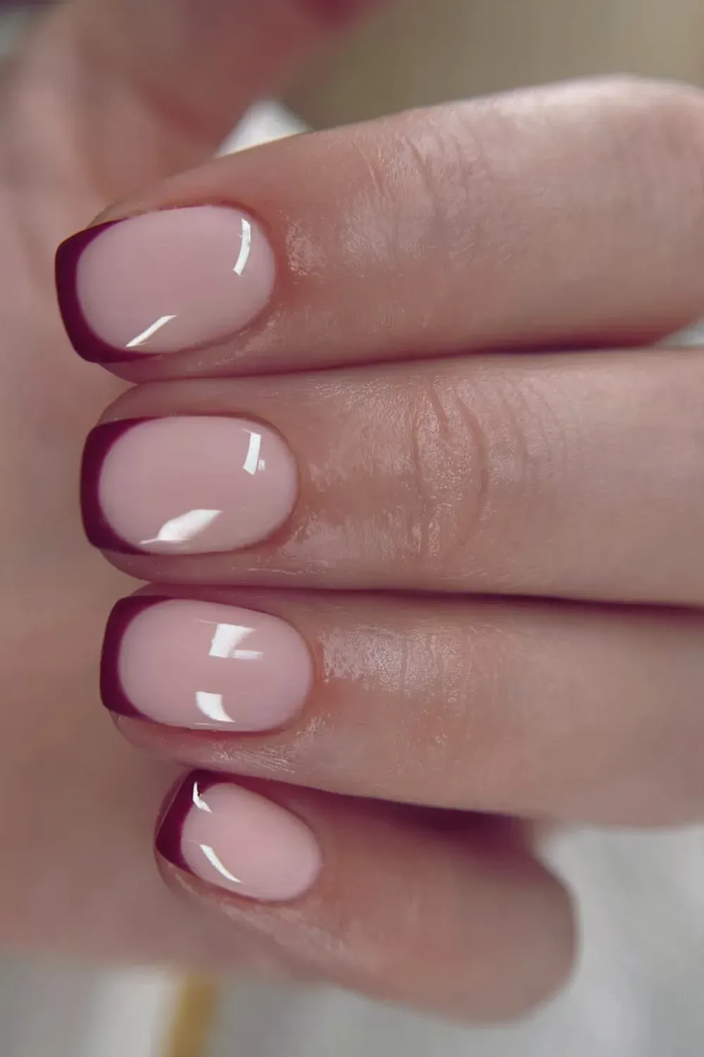 Short oval nails with a super thin, dark burgundy-red micro-French tip on a glossy pink nude base.